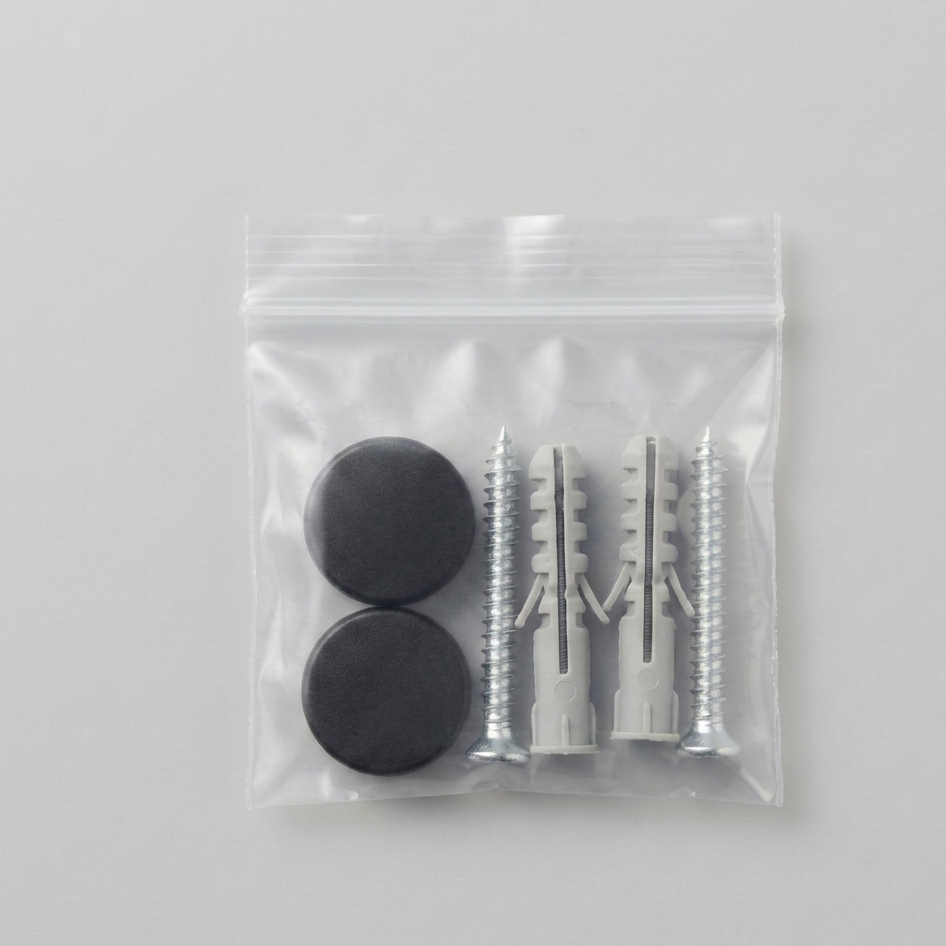 A clear plastic zip-top bag containing two round black magnets and two silver wall anchors, photographed on a light gray background.