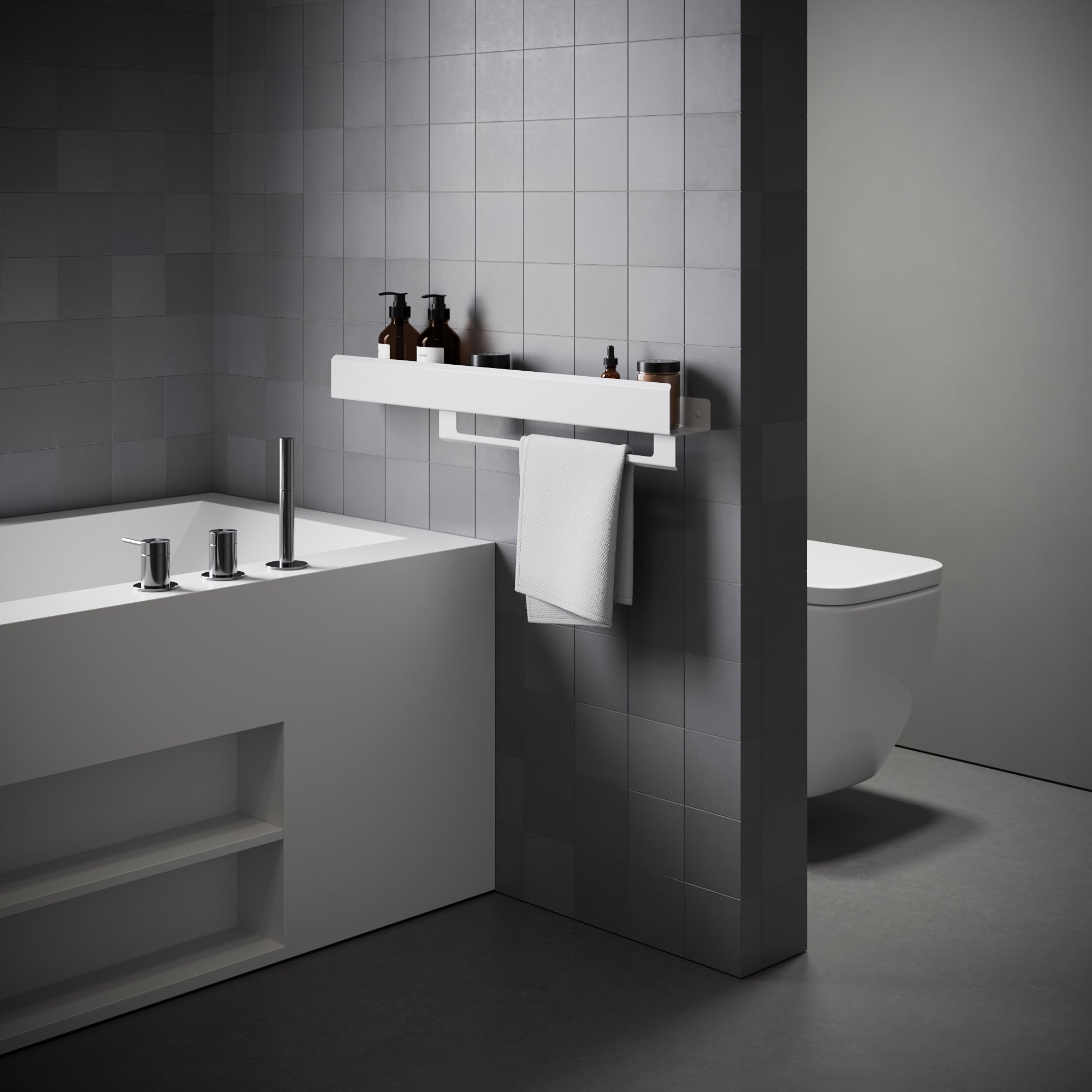 Modern bathroom interior with a white wall-mounted shelf holding small bottles and a white towel, beside a white bathtub and a partially visible white toilet. The space is styled with dark gray square wall tiles and a dark floor.